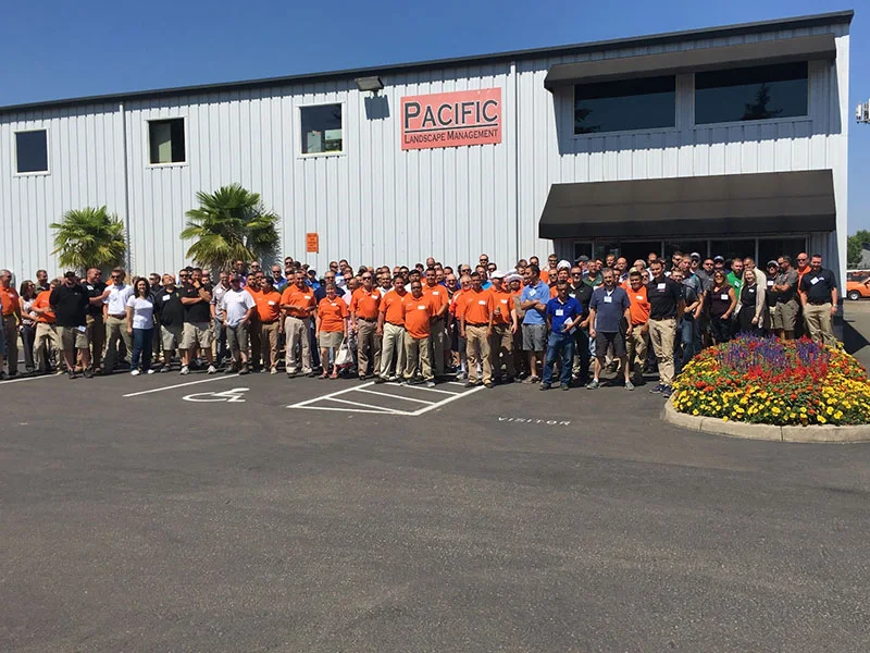 A large group of people, some wearing orange shirts, standing outside a building with a sign that reads